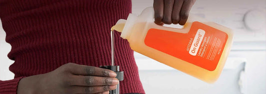 Mains versant la lessive liquide On Guard dōTERRA dans son bouchon doseur, devant un pull bordeaux