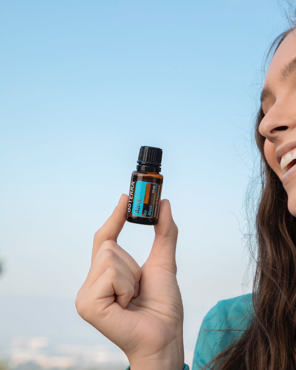 Air-X mélange d'huiles essentielles dōTERRA, flacon tenu en main sur fond de ciel