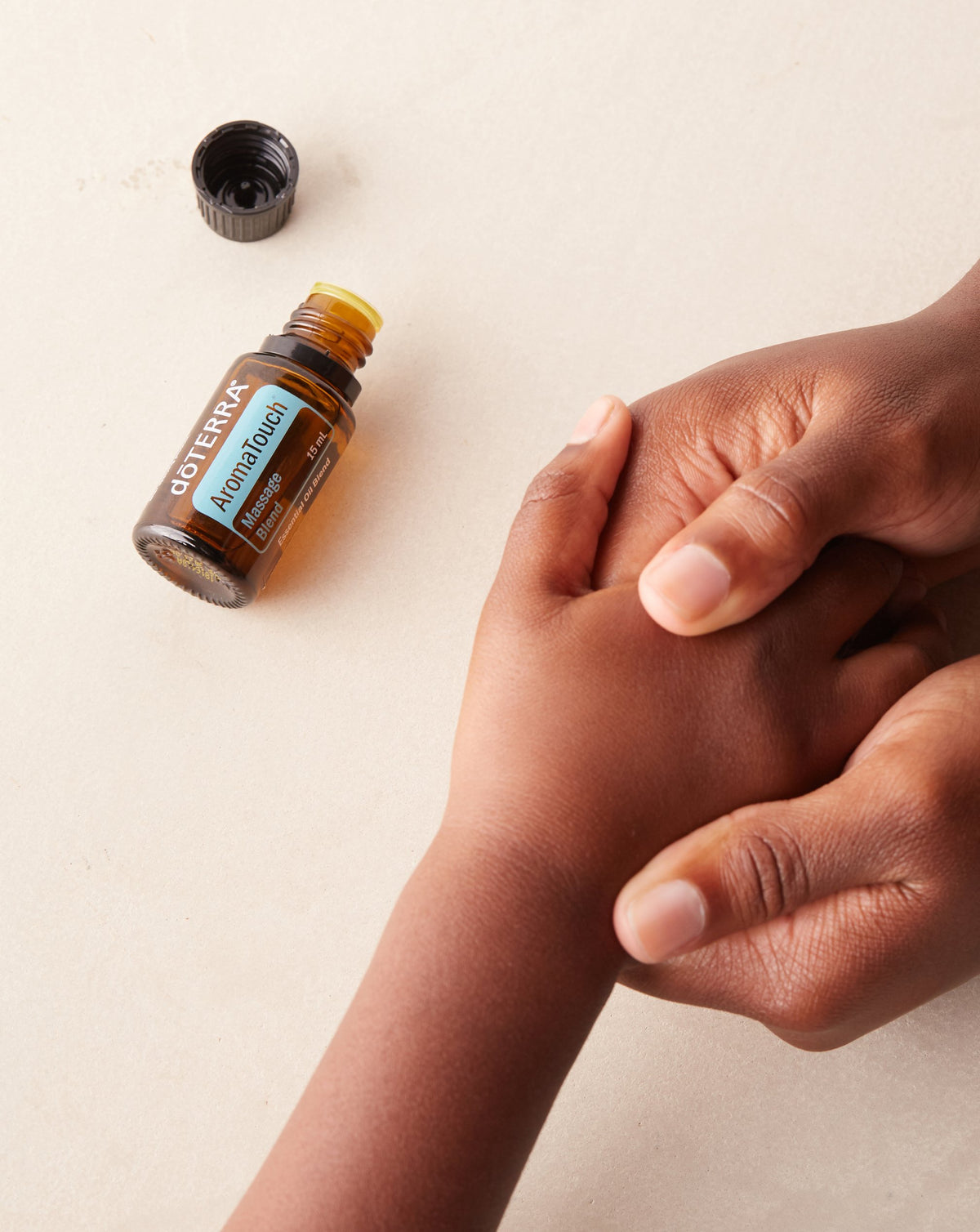 AromaTouch mélange d'huiles essentielles dōTERRA, flacon et mains sur fond beige