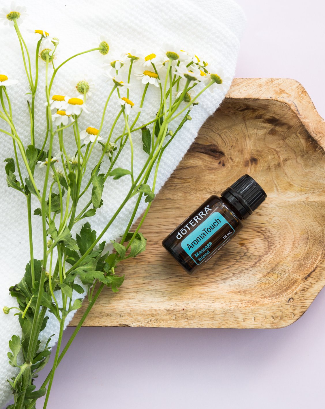 AromaTouch mélange d'huiles essentielles dōTERRA, flacon sur un plateau en bois avec de la camomille