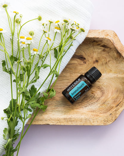 AromaTouch mélange d'huiles essentielles dōTERRA, flacon sur un plateau en bois avec de la camomille