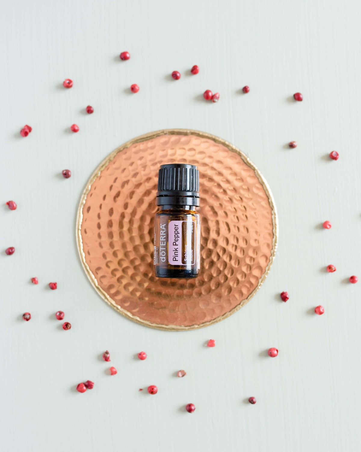 Baies roses huile essentielle dōTERRA, sur une assiette en paille parsemée de baies roses