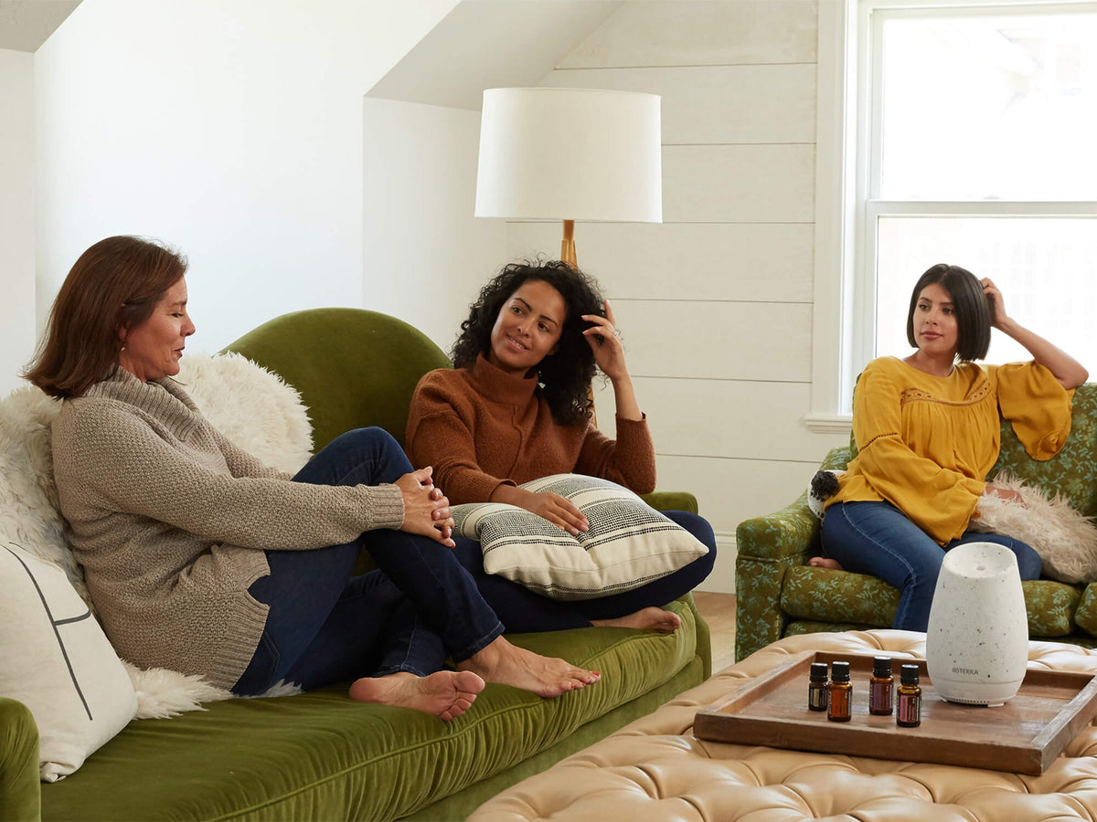 Trois amies discutent dans un salon, un diffuseur et des flacons d'huiles essentielles dōTERRA sur la table