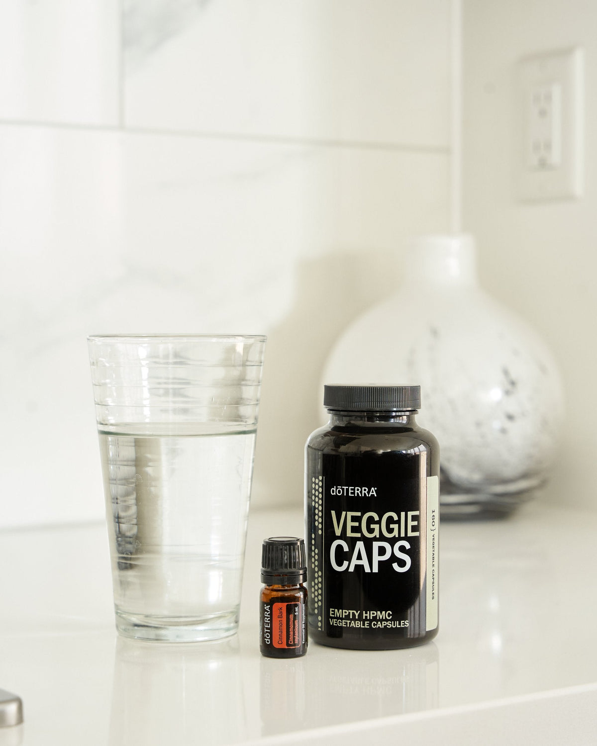 Écorce de cannelle huile essentielle dōTERRA, avec un pot de gélules et un verre d'eau