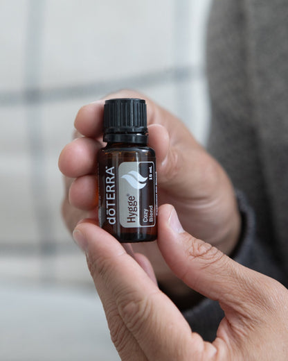 Hygge mélange d'huiles essentielles dōTERRA, flacon tenu en main, ambiance cocooning