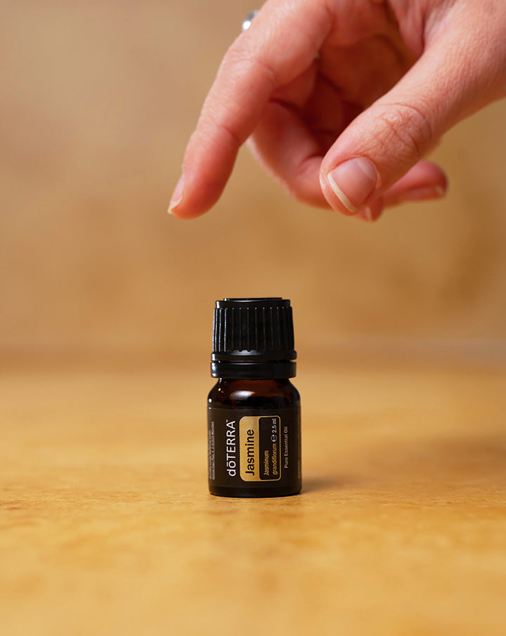 Main s'approchant d'un flacon d'huile essentielle de Jasmin dōTERRA