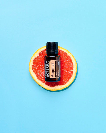 Pamplemousse huile essentielle dōTERRA, sur une moitié de pamplemousse, fond bleu