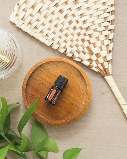 Thuya huile essentielle dōTERRA, flacon sur un plateau en bois et un éventail tressé